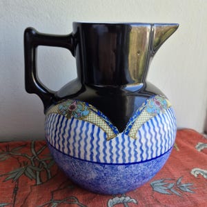 Może przedstawiać: Czarny i niebieski dzbanek ceramiczny z dekoracyjnym wzorem kwiatowym. Dzbanek ma okrągłe ciało i szeroki dzióbek.