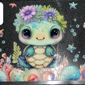 May include: A whimsical illustration of a sea turtle with large, purple-eyed, and a floral crown. The design features a black background with sea life elements like starfish, seashells, and bubbles. The number "#2" is in a white square.