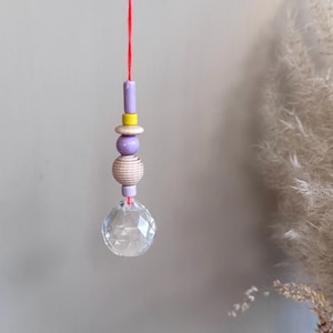 May include: A crystal prism hanging from a red string with purple, yellow, and white beads.