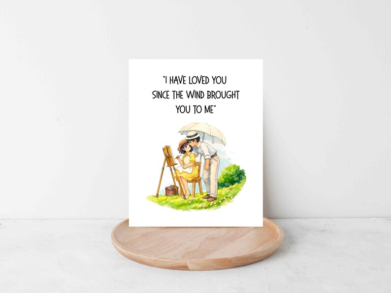 Może przedstawiać: Kartka okolicznościowa z ilustracją pary pod parasolem. Kobieta maluje na sztaludze. Na kartce widnieje napis: "I HAVE LOVED YOU SINCE THE WIND BROUGHT YOU TO ME."