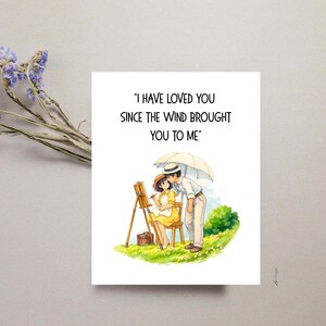 Może przedstawiać: Biała kartka z pozdrowieniami z napisem "I HAVE LOVED YOU SINCE THE WIND BROUGHT YOU TO ME" przedstawia ilustrację pary pod parasolem. Kobieta maluje na sztaludze. Suszone niebieskie kwiaty w lewym g&oacute;rnym rogu.