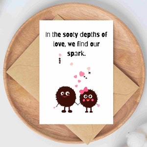 May include: A greeting card with the text "In the sooty depths of love, we find our spark." features two cartoon characters holding hands. The card is on a wooden tray with a brown envelope.