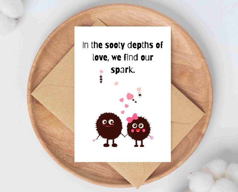 May include: A greeting card with the text "In the sooty depths of love, we find our spark." features two cartoon characters holding hands. The card is on a wooden tray with a brown envelope.