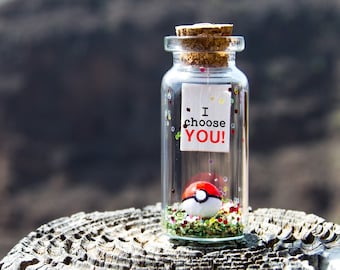 May include: A small glass jar with a cork lid filled with glitter and a small red and white Pokeball. The jar has a white paper note attached to it that says "I choose YOU!"