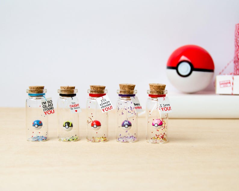 May include: Five small clear glass bottles with cork stoppers, each containing a miniature spherical toy and colorful glitter. Each bottle features a small white tag with printed text including phrases like I'm so glad I found you and I love you.