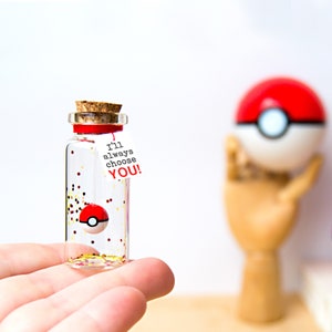 May include: A small clear glass bottle with a cork stopper containing a miniature red and white ball, gold and red glitter, and a white paper tag tied with a red string that features the black and red text I'll always choose YOU!
