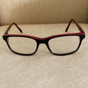 May include: Black eyeglasses with a red rim. The glasses have a rectangular shape and are made of plastic.
