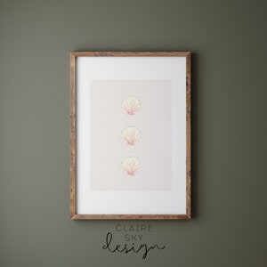May include: A framed print with three stylized pink and yellow seashells in a vertical line. The print is on a light beige background. The frame is brown wood. The text below the print reads 'CLAIRE SKY design'.
