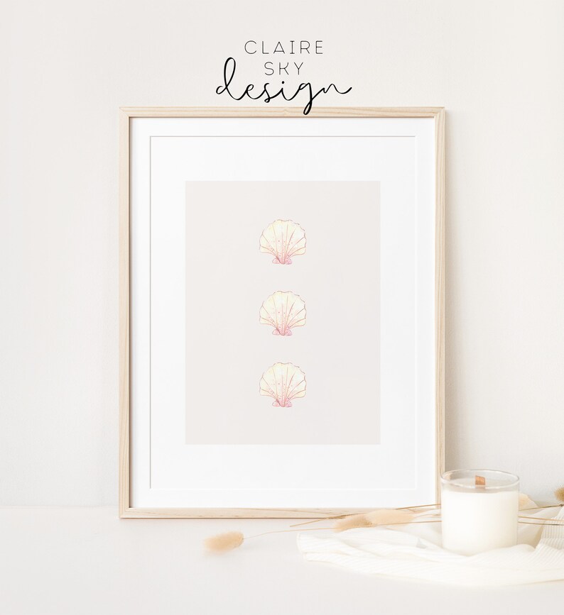 May include: A framed print with three pink and yellow seashells on a light beige background. The frame is light wood and the text 'CLAIRE SKY design' is at the top of the print.