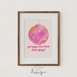 Puede incluir: Impresi&oacute;n art&iacute;stica enmarcada con una bola de discoteca rosa y magenta y el texto "you guys ever think about dying?". La obra de arte est&aacute; sobre un fondo rosa claro y enmarcada en un marco de madera marr&oacute;n.
