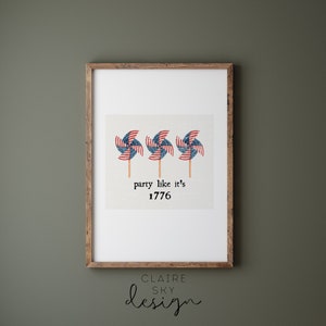 Op de afbeelding: Een ingelijste print met drie windmolens met het ontwerp van de Amerikaanse vlag. De tekst "party like it's 1776" staat onder de windmolens.