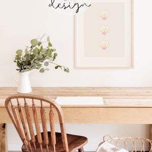 May include: A framed print with three pink and white seashells on a light gray background. The frame is light wood and the print is hanging on a white wall. There is a wooden table with a white pitcher and greenery in front of the print. A wooden chair and a white blanket are on the table.