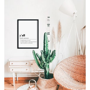 May include: A black framed print with the word "y'all" in bold, followed by the definition: "[yawl] pronoun 1. an abbreviation of "you all" 2. a southern expletive, expressing excitement, anger, frustration, or astonishment"