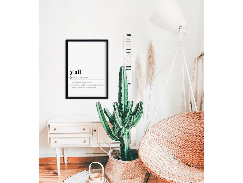 May include: A black framed print with the word "y'all" in bold, followed by the definition: "[yawl] pronoun 1. an abbreviation of "you all" 2. a southern expletive, expressing excitement, anger, frustration, or astonishment"