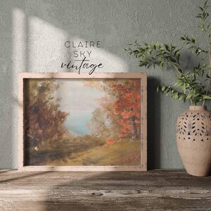 Puede incluir: Una pintura de paisaje vintage enmarcada con un cielo azul claro, &aacute;rboles verdes y un r&iacute;o en la distancia. La pintura est&aacute; en un marco de madera claro y est&aacute; colgada en una pared.