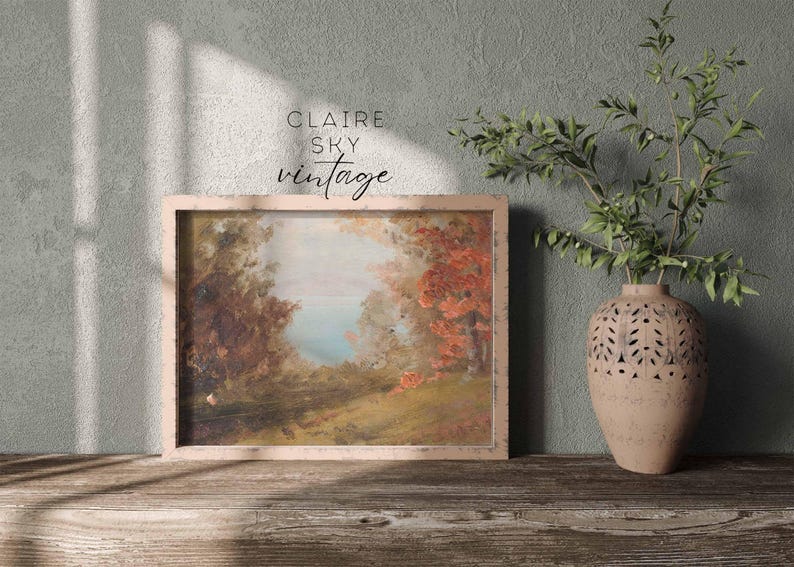 Puede incluir: Una pintura de paisaje vintage enmarcada con un cielo azul claro, &aacute;rboles verdes y un r&iacute;o en la distancia. La pintura est&aacute; en un marco de madera claro y est&aacute; colgada en una pared.