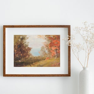 Puede incluir: Una pintura enmarcada que representa una escena de paisaje con &aacute;rboles, una masa de agua y una zona herbosa. Los &aacute;rboles son una mezcla de verde y rojo, y el agua es de un azul claro. La pintura est&aacute; en un marco de madera marr&oacute;n.