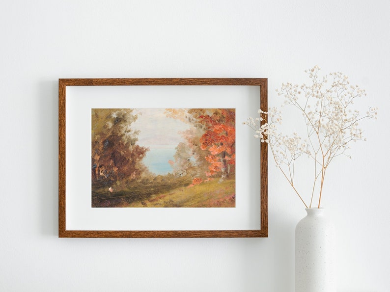 Puede incluir: Una pintura enmarcada que representa una escena de paisaje con &aacute;rboles, una masa de agua y una zona herbosa. Los &aacute;rboles son una mezcla de verde y rojo, y el agua es de un azul claro. La pintura est&aacute; en un marco de madera marr&oacute;n.