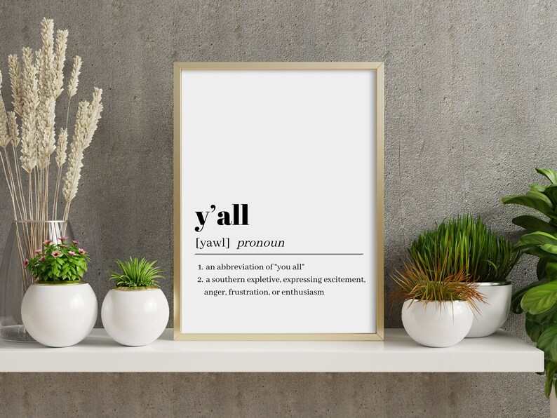 May include: A framed print with a white background and black text. The text defines the word "y'all" as a pronoun, an abbreviation of "you all", and a southern expletive expressing excitement, anger, frustration, or enthusiasm.