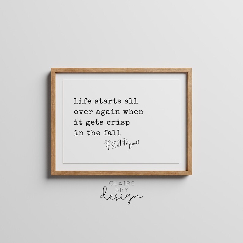 May include: A framed print with a quote by F. Scott Fitzgerald that reads "life starts all over again when it gets crisp in the fall". The print is on a white background and has a brown wooden frame. The text "CLAIRE SKY design" is printed below the quote.