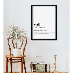 May include: A black framed print with a white background and the word "y'all" in bold black text. The definition of the word is written in smaller black text below. The definition is: "[yawl] pronoun 1. an abbreviation of 'you all' 2. a southern expletive, expressing excitement, anger, frustration, or enthusiasm"