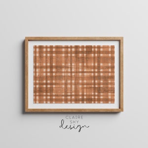Puede incluir: Una impresión enmarcada con un patrón de cuadros marrones y blancos. El marco es de madera clara. La impresión tiene un aspecto desgastado, con el patrón de cuadros que parece descolorido y usado. La impresión está titulada "CLAIRE SKY design".