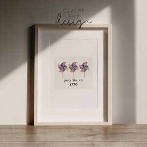 Op de afbeelding: Een ingelijst print met een witte achtergrond en drie rood-wit-blauwe windmolens. De tekst "party like it's 1776" staat onder de windmolens.