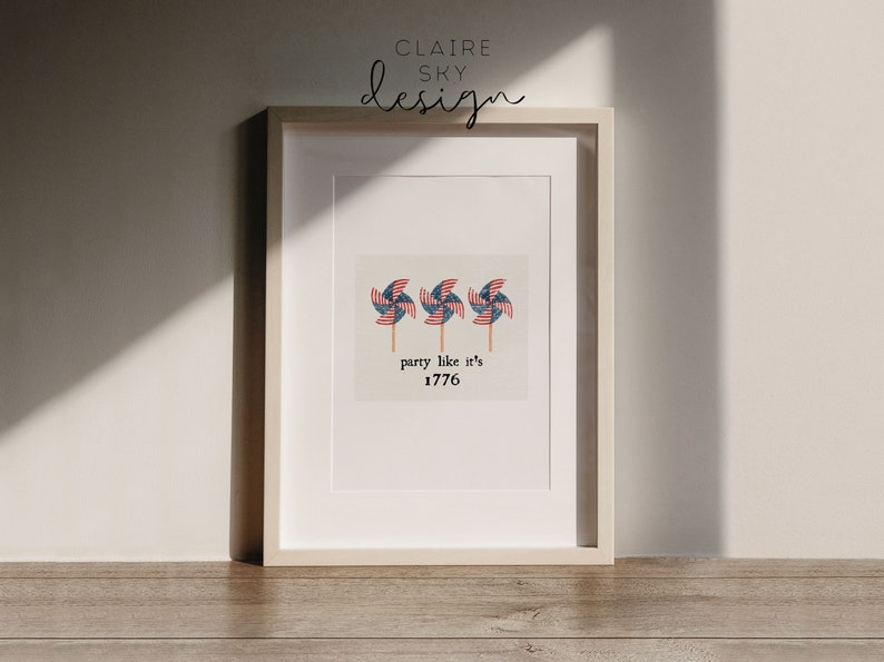 Op de afbeelding: Een ingelijst print met een witte achtergrond en drie rood-wit-blauwe windmolens. De tekst "party like it's 1776" staat onder de windmolens.