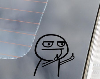 May include: A black vinyl sticker of a meme character giving the middle finger, applied to the rear window of a vehicle. The sticker is a simple line drawing with a white background. The window has defroster lines.