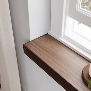 May include: A close-up of a wooden window sill with a white candle and a green plant on top. The window sill is made of dark wood with a natural grain pattern.