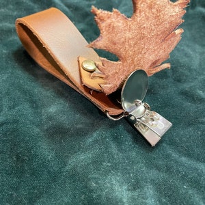 May include: A brown leather keychain with a metal clip and a brown leather leaf charm.