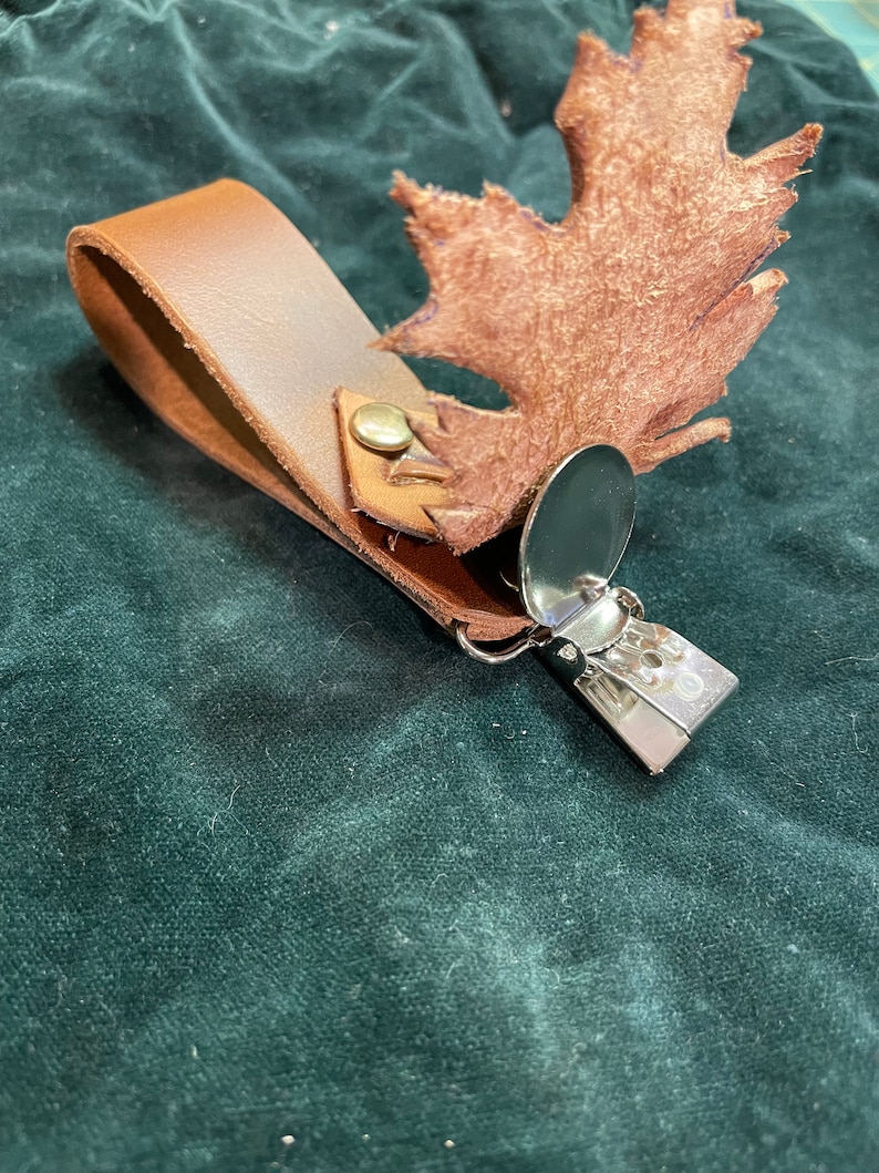 May include: A brown leather keychain with a metal clip and a brown leather leaf charm.
