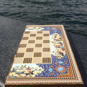 May include: A decorative wooden chess board with a detailed, colorful design. The board features a checkered playing surface, intricate floral patterns, and illustrations of figures on horseback. The edges are trimmed with a gold border.