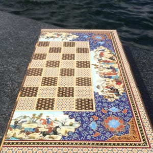 May include: An ornate, rectangular chess and backgammon board. The board features a checkerboard pattern, detailed illustrations, and intricate floral designs in shades of blue, brown, and orange. The board is set against a dark background.