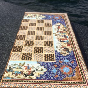 May include: An intricately decorated game board with a checkerboard and detailed illustrations. The board has a blue floral design, a patterned border, and scenes of people on horseback. The board is rectangular.