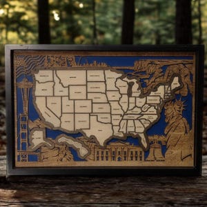 May include: A framed wooden map of the United States, laser-cut with state outlines and iconic landmarks. The map features a blue background and a black frame, showcasing the country's geography and famous monuments.