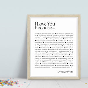 Può includere: Una stampa incorniciata con il testo "I Love You Because..." in nero. La stampa presenta un elenco di motivi per cui qualcuno è amato, con una cornice in legno chiaro. Coriandoli colorati sparsi in basso.