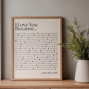 以下が含まれることがあります： 「I Love You Because...」というテキストが黒字で書かれた額入りのプリント。テキストは小さなハートのシンボルで囲まれています。プリントは明るい茶色の木製フレームに入っており、木製の表面に表示されています。
