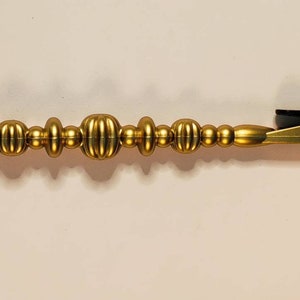 May include: A gold-coloured metal clip with a beaded handle. The beads are round and have a textured surface.