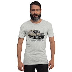 May include: A grey t-shirt featuring a beige Toyota Land Cruiser 70 series with a roof top tent. The vehicle is illustrated in a cartoon style. The text "Legends Never Die" is printed below the vehicle.