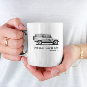May include: White ceramic mug featuring a black and white illustration of a Land Rover Defender 110. The mug has the text "Legends Never Die" and "LR Defender 110" printed on it.