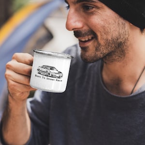 Może przedstawiać: Biały kubek emaliowany z czarno-białym rysunkiem samochodu i tekstem "Born To Street Race".