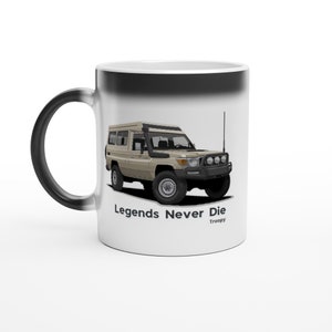 May include: A white ceramic coffee mug with a black interior. The mug features a black and white illustration of a Toyota Land Cruiser with the text "Legends Never Die" and "Troopy" below the image.