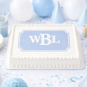 May include: A rectangular white cake with a light blue monogram that reads "WBL" is the centerpiece of a party scene. The cake is surrounded by party supplies in shades of blue and white, including balloons, plates, and party hats.