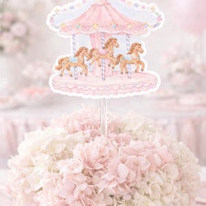 May include: A pink and white floral arrangement topped with a carousel-themed decoration. The carousel has a pink canopy with star accents and features three brown horses. The overall aesthetic is soft and pastel.