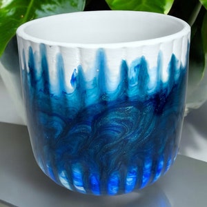 May include: A white ceramic planter with a blue and white marbled design. The planter has a textured surface and a wide opening.