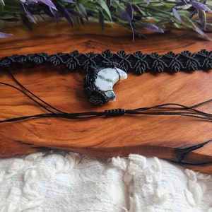 May include: A black macrame choker necklace with a crescent moon shaped green and white agate pendant.