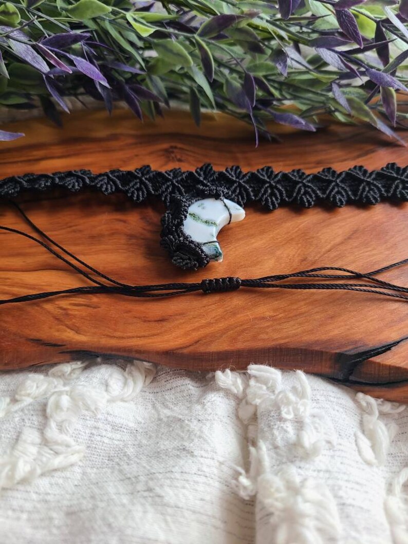 May include: A black macrame choker necklace with a crescent moon shaped green and white agate pendant.