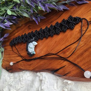 May include: A black macrame choker necklace with a white and green stone pendant. The necklace is tied with black cord and has white beads on the ends.