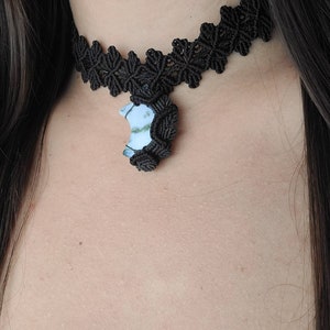 May include: A black choker necklace with a crescent moon pendant. The pendant is made of white and green agate.